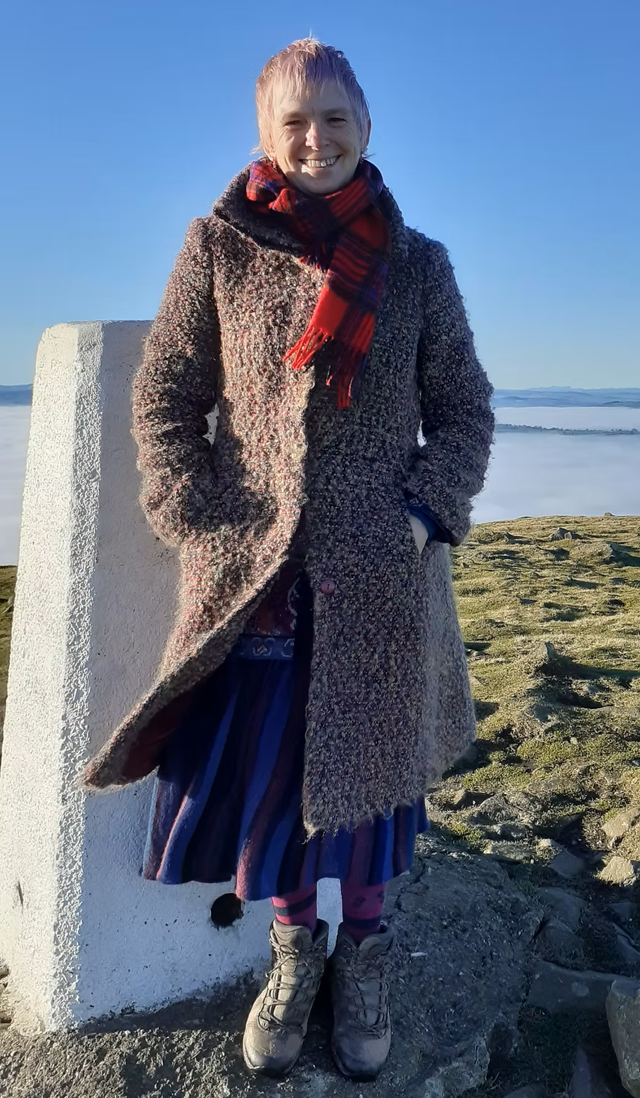 Rachael Davenhill
is stood by a trig point atop a hill in the UK